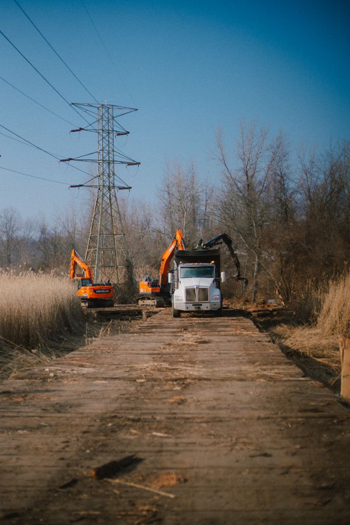 Crews loading swamp mats onto a timber access road with excavators and a knuckleboom truck